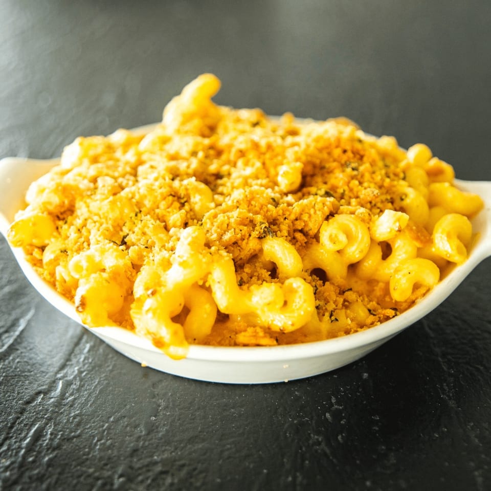 A white bowl filled with golden-brown macaroni and cheese, topped with crispy breadcrumbs, on a dark surface.