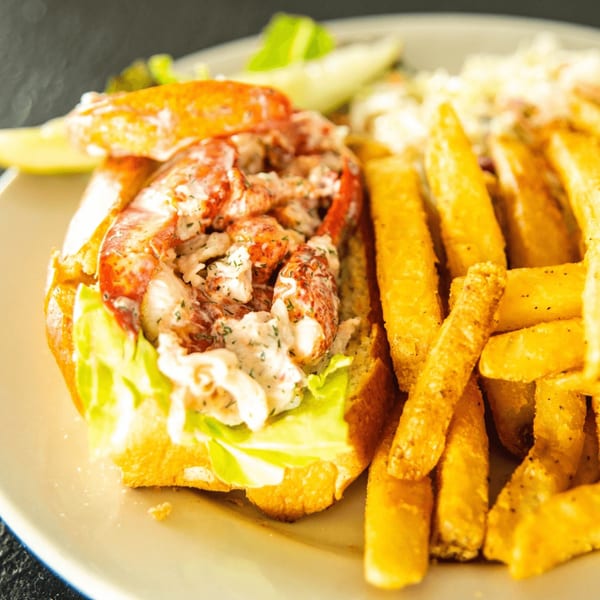 A Localz Kitchen and Cocktails lobster roll with fries and coleslaw on a white plate.