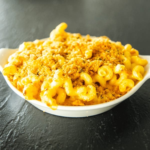 A white bowl filled with golden-brown mac and cheese, topped with crispy breadcrumbs, on a dark surface.