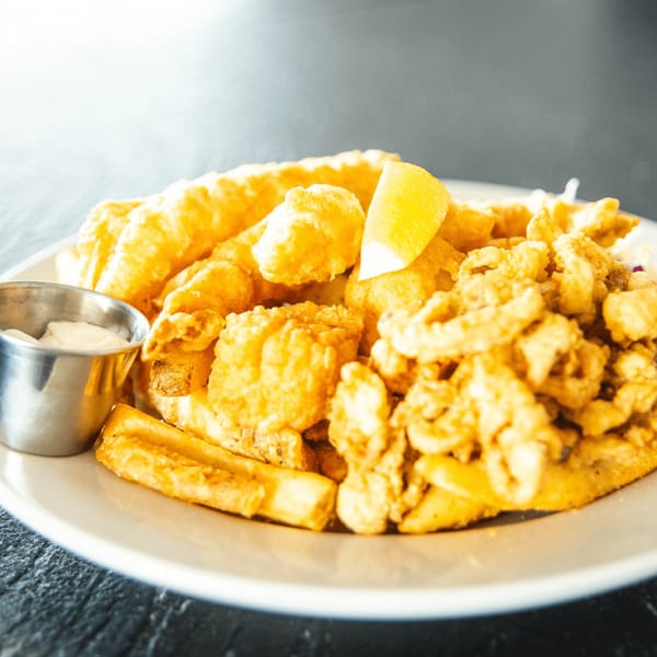 A large platter of golden-fried fish, calamari, and french fries with a side of tartar sauce.