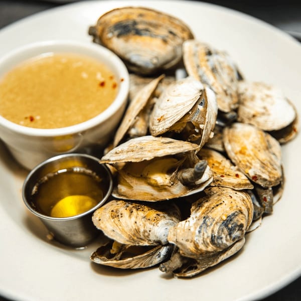 Steamed clams with two dipping sauces, one in a white ramekin and the other in a metal cup.